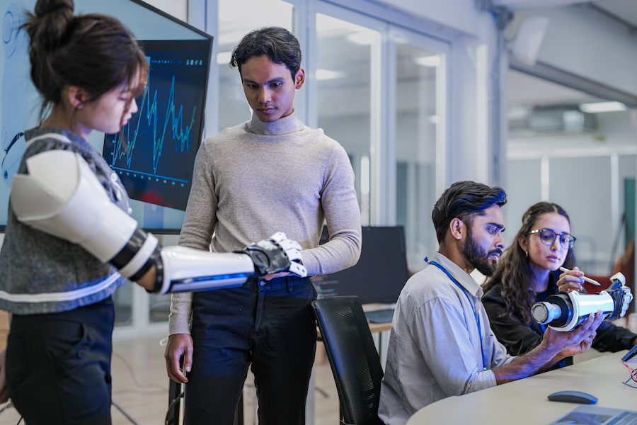 A robotics team develops a new bionic limb, inspecting the prototype while analyzing real-time performance data. A concept for digital twins, agile R&D, and mechatronics innovation.